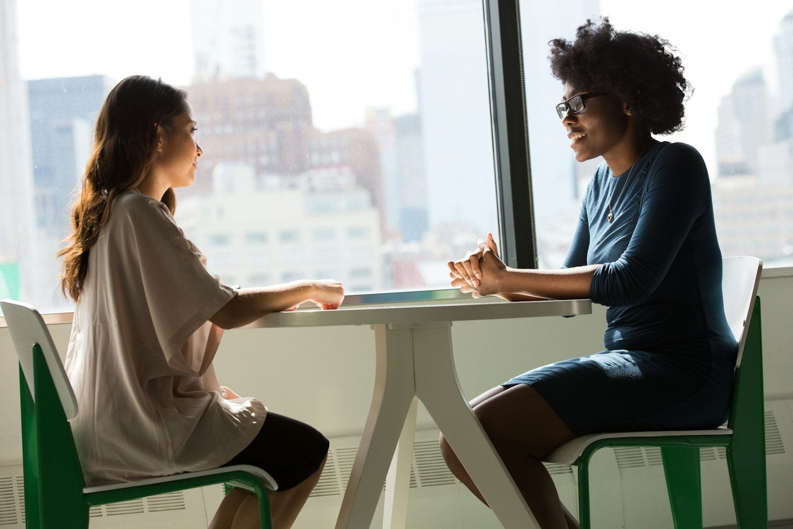 Two women talking across a table in an office.
